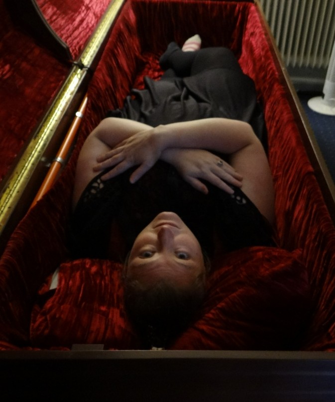 Nicole Holmes reclining in a red-lined coffin.